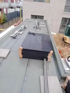 Začiatok montáže fotovoltaiky na plochej streche – pripravené solárne panely, konštrukcie a náradie na montáž.