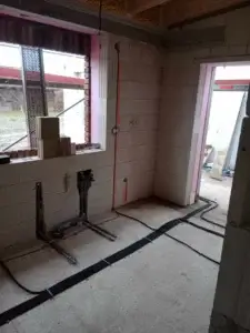 Electrical cabling in kitchen near window, mounted on fresh concrete floor.